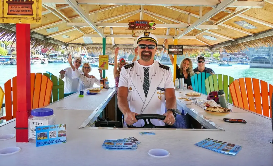 a man in a uniform sitting at a table with people in the background - boat rental